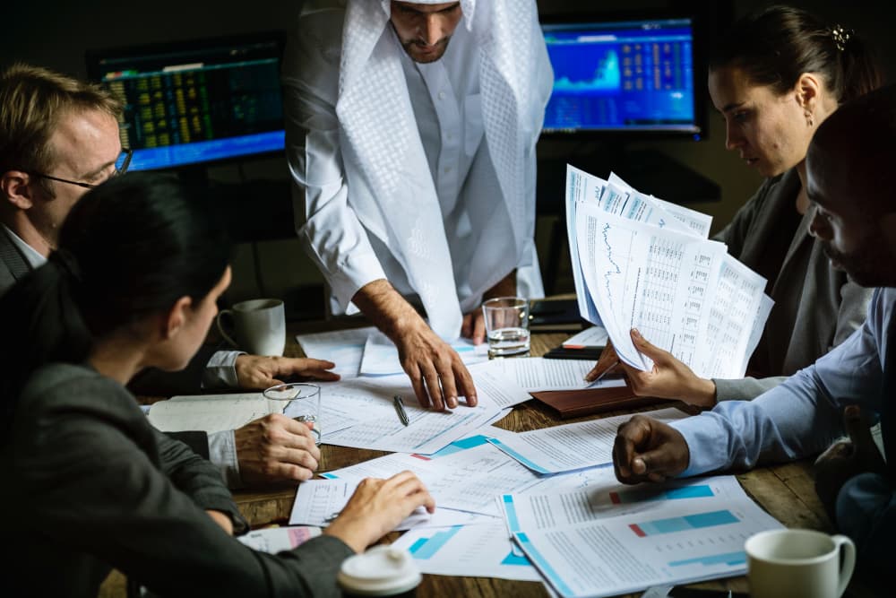 A diverse team of professionals reviews financial reports and charts during a focused business meeting.