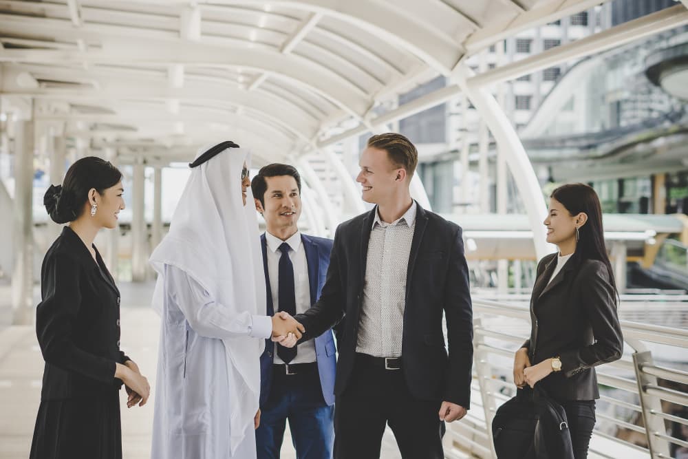A group of business professionals are smiling and shaking hands outdoors in a modern urban setting.